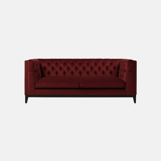 That’s a burgundy tufted sofa with a deep-buttoned back and sides — a design that resembles a modern Chesterfield. It has two seat cushions, straight square arms, and a solid dark wood base with tapered legs.