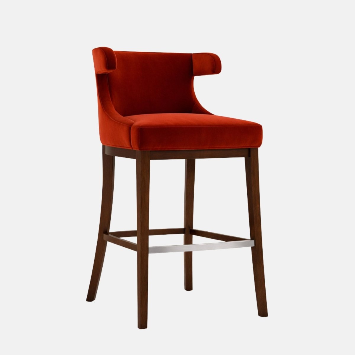 Three-quarter view of a bar-height stool upholstered in burnt orange/rust velvet with a wide seat and curved wraparound back/arms featuring small rolled “ear” ends at the top, on a dark wood four-leg frame with square stretchers and a brushed metal foot rail, photographed on a white background.