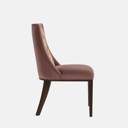 Upholstered dining chair in muted mauve fabric with a cushioned seat and angled backrest, featuring a pink botanical and bird-patterned fabric panel, supported by dark wooden legs, shown on a white background