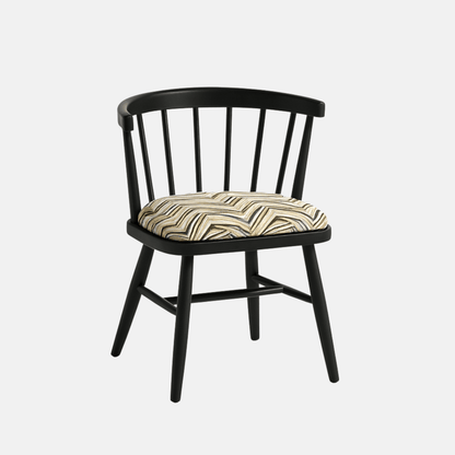 A modern black Windsor-style chair with a curved spindle backrest and four angled legs, featuring a cushioned seat upholstered in a geometric zigzag fabric with neutral tones. The chair is photographed against a light beige background with soft shadows for a clean, realistic presentation.
