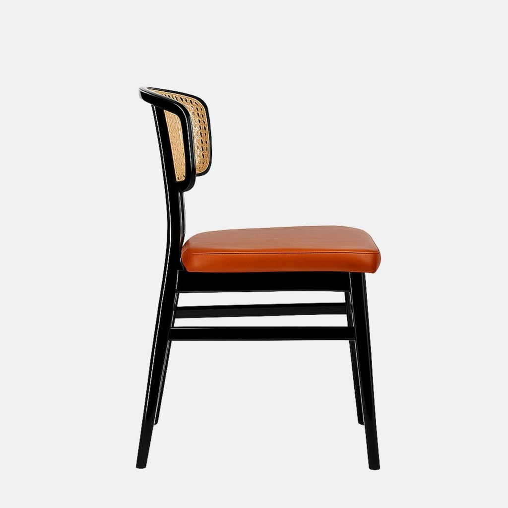 Contemporary dining chair with a black wooden frame, natural cane backrest, and a square padded seat upholstered in burnt orange leather. The design combines mid-century and modern styles