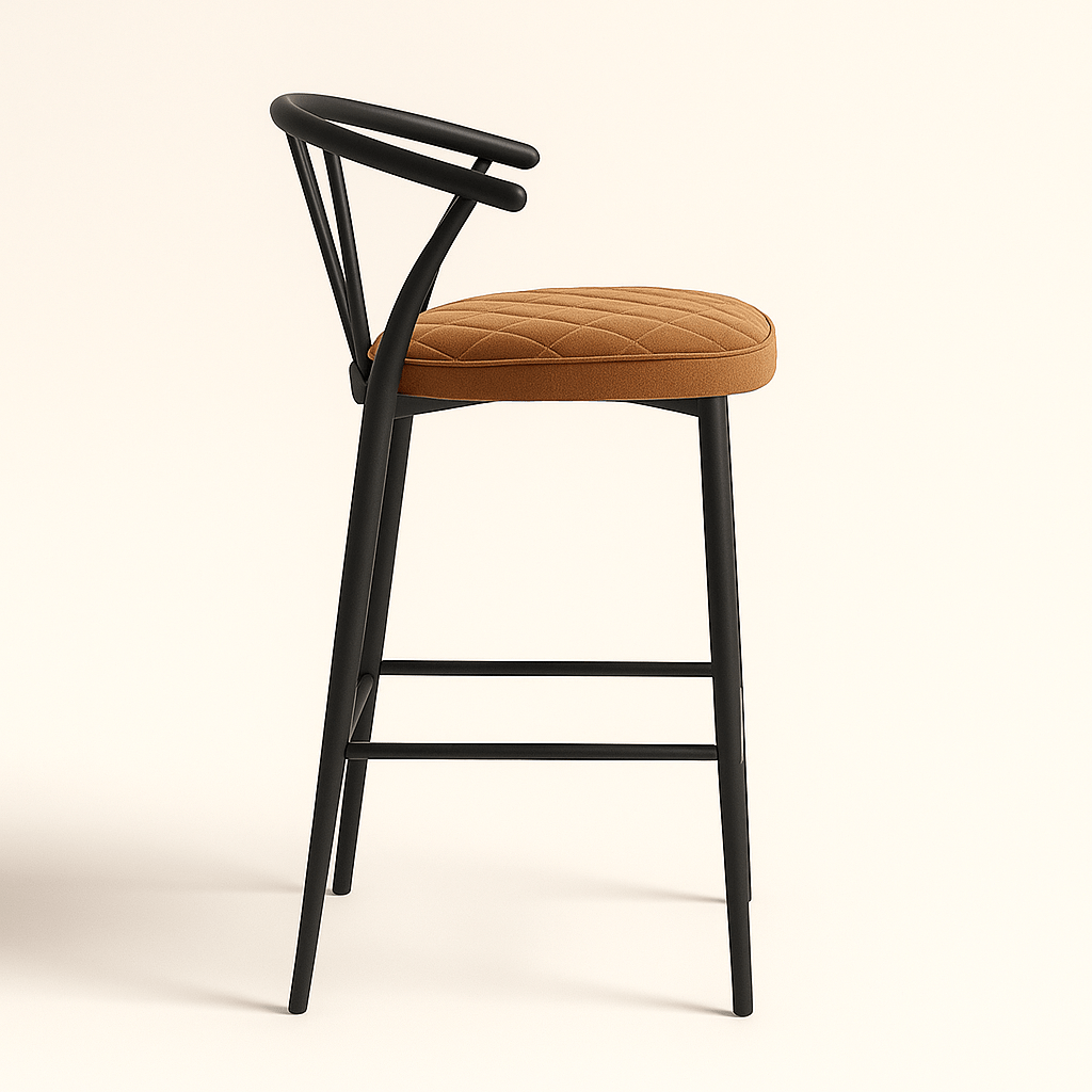 A modern bar stool featuring a matte black wooden frame with slender, tapered legs and a curved, open backrest supported by vertical spindles. The seat is upholstered in tan velvet with a diamond stitch pattern, adding a touch of texture and elegance. A sleek metal footrest completes the contemporary design.