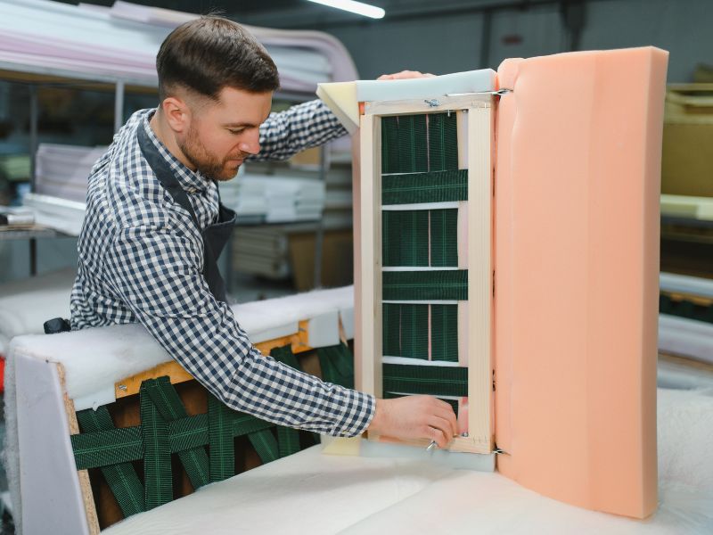 Upholsterer installing springs and foam padding on a sofa frame in a furniture workshop