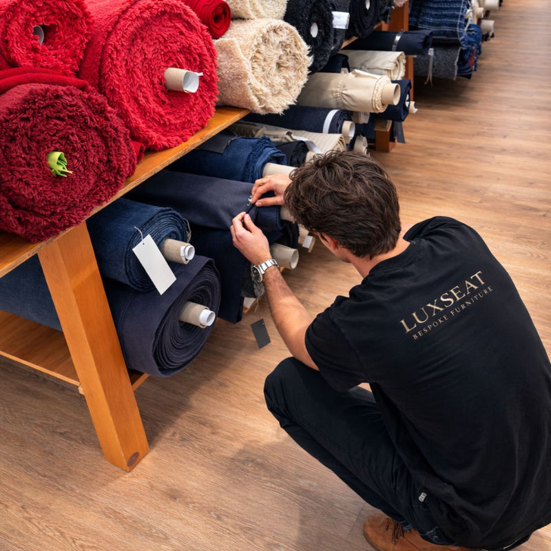 Person selecting upholstery fabric rolls in a furniture workshop.