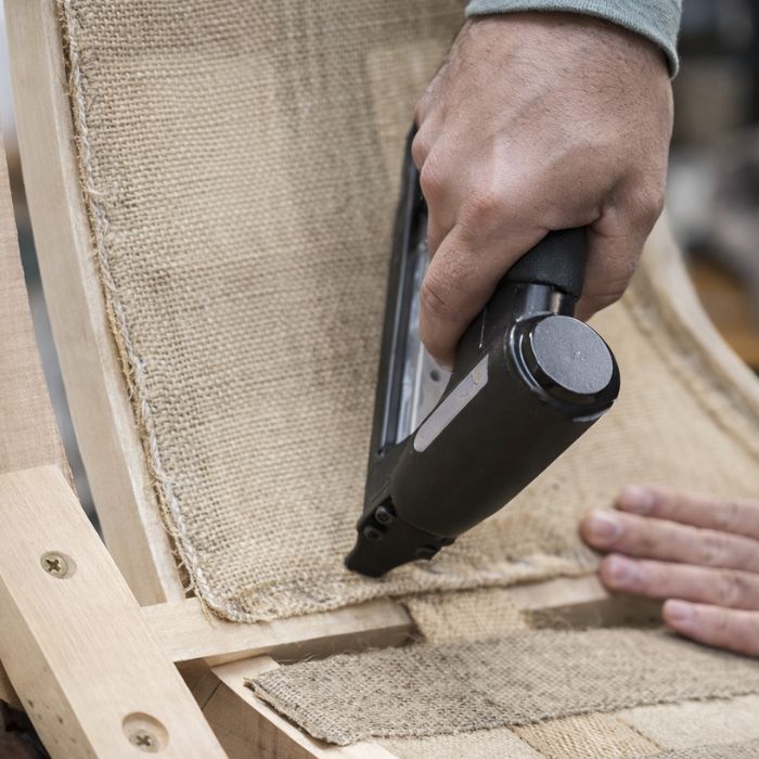 Close-up of upholstery process with staple gun fixing fabric to a wooden chair frame in furniture manufacturing
