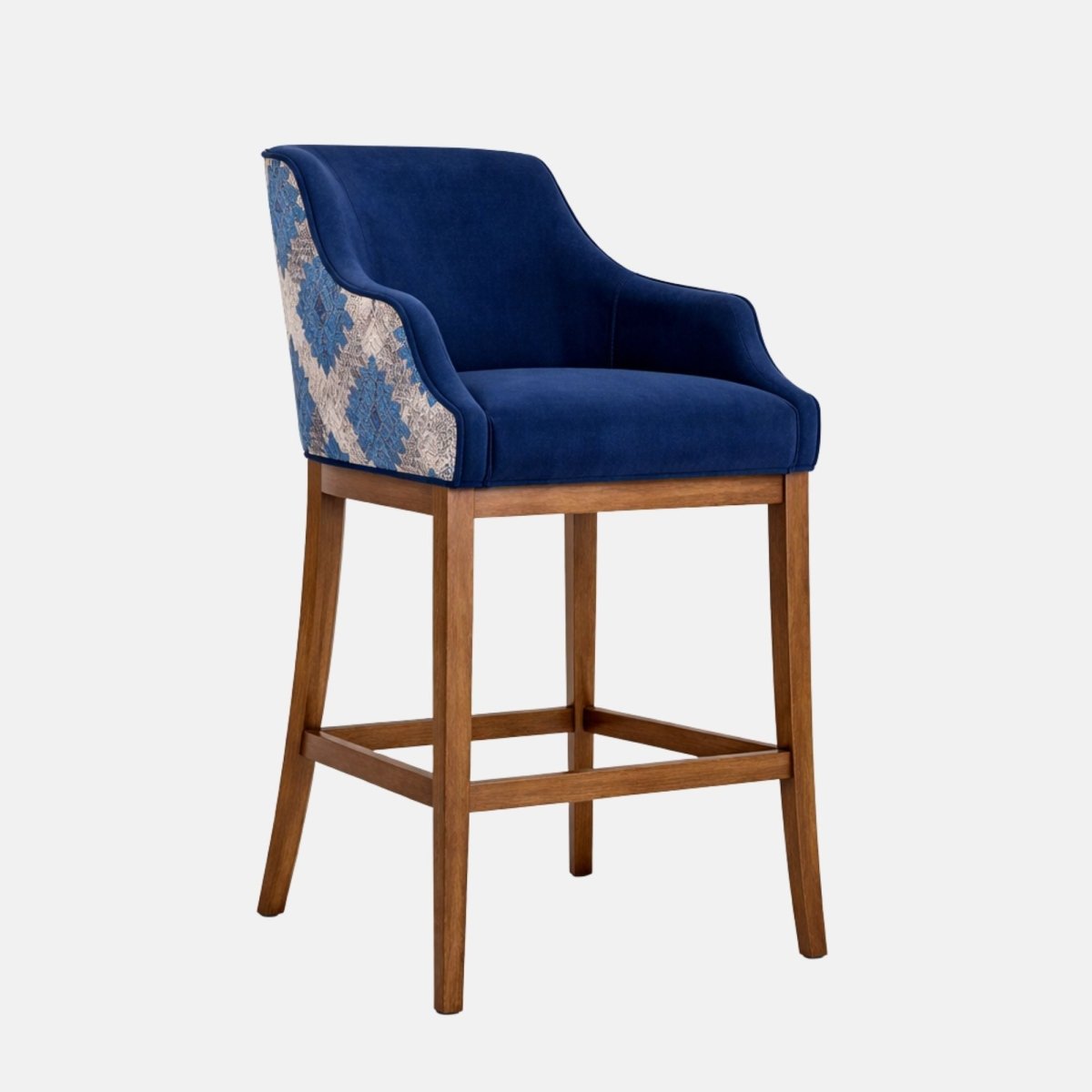 Front angled view of a bar-height stool with a navy upholstered seat and wraparound back/arms, patterned blue-and-cream fabric on the outer back panel, and a medium-brown wooden frame with four legs and a square footrest stretcher, photographed on a white background.
