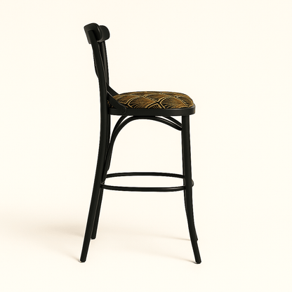 A modern black wooden barstool with an X-shaped backrest and gently curved legs, featuring a round cushioned seat upholstered in a gold and brown Art Deco patterned fabric, set against a plain beige background with a soft shadow.